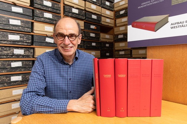 Robert Damme in seinem Arbeitszimmer mit allen fünf Bänden des Westfälischen Wörterbuchs und dem Beiband (2021)