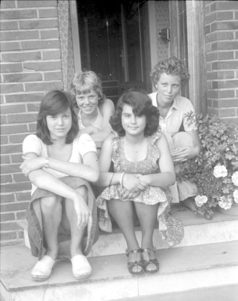Schwarz-weiß Foto von 4 Mädchen, die vor einer offenen Haustür auf der Treppe sitzen
