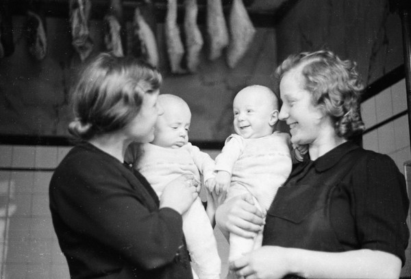 Zwei Frauen halten Babys hoch. Das linke Baby schaut traurig drein, das rechte grinst. Foto: Böckenhoff, Ignaz; LWL-Medienzentrum für Westfalen.