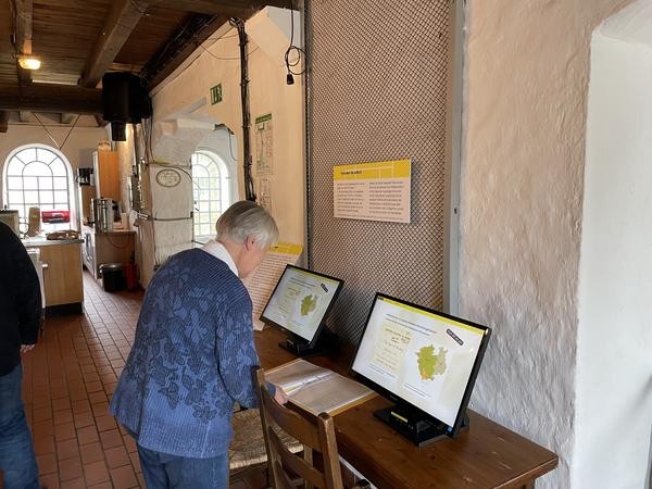 Besucherin schaut sich Kartenabbildungen auf einem Monitor an